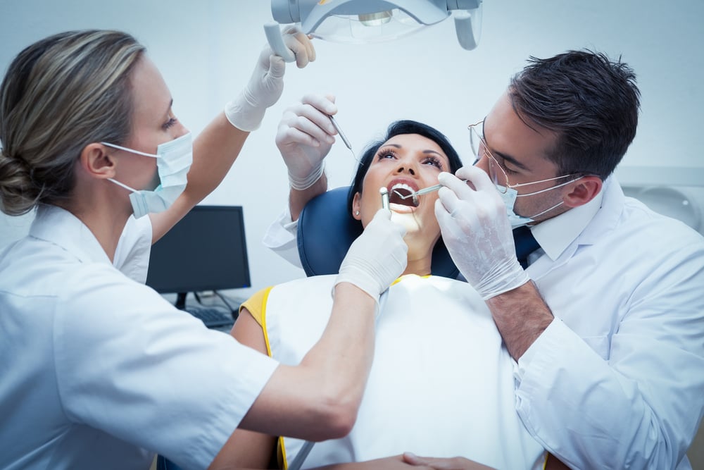 Male dentist with assistant examining womans teeth in the dentists chair
